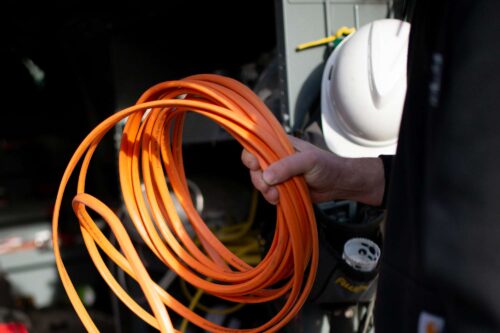 hand holding orange electrical wires with hard hat in background