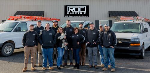 roc electric team standing outside roc building with trucks